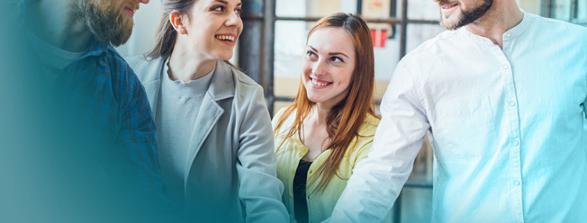 4 Phasen der Teamentwicklung: Zwei Frauen und zwei Männer in hellem Business-Outfit vereinen ihre Hände in der Mitte als Symbol für Teamspirit und Zusammenarbeit.