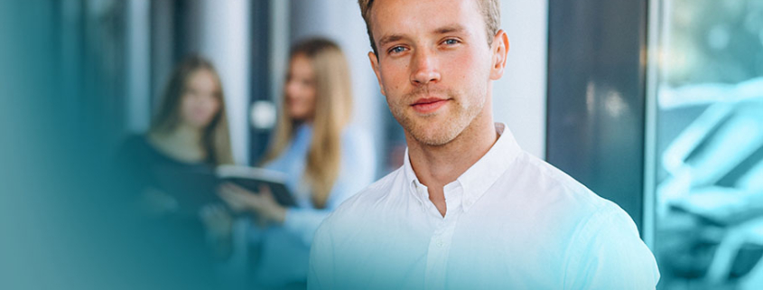 Erfolgreich vom Experten zur Führungskraft: Junger Mann mit Führungspotenzial in Büroumgebung. Sein direkter Blick und die aufrechte Haltung strahlen Kompetenz und Entschlossenheit aus.