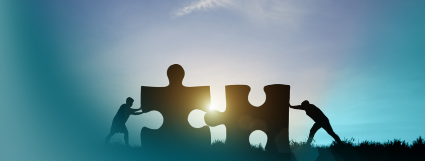 Shared Leadership: Harmonisches Zusammenspiel zweier Personen beim Verbinden riesiger Puzzleteile im Sonnenlicht – Sinnbild moderner Führungskonzepte.