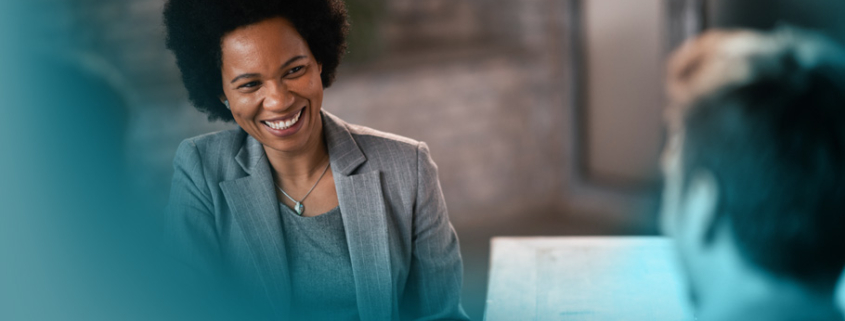 CRM im Vertrieb: Eine professionelle Beraterin im grauen Anzug bespricht in entspannter Atmosphäre wichtige Dokumente mit zwei Gesprächspartnern.