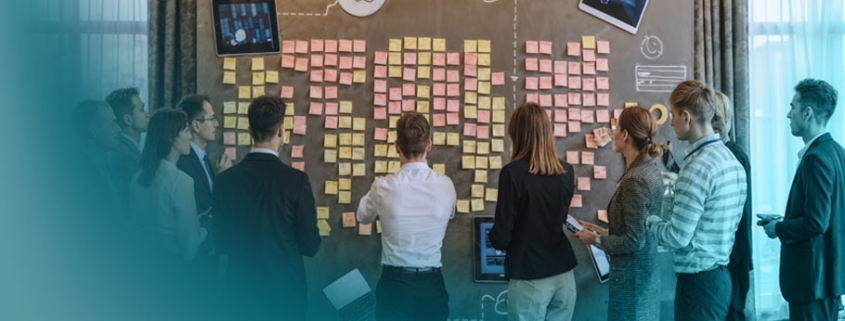 Stakeholdermanagement im Projekt: Geschäftsleute analysieren gemeinsam eine Wand voller Post-its und Notizen während eines strategischen Planungsmeetings.