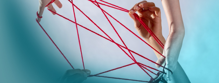 Komplexität im Projektmanagement: Mehrere Hände halten ein rotes Fadennetzwerk vor hellem Hintergrund - symbolisiert Vernetzung und Zusammenarbeit in komplexen Projekten.