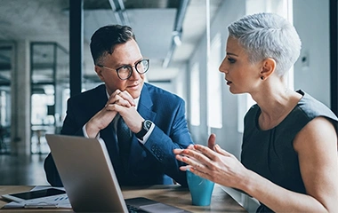 Geschäftsfrau mit kurzen Haaren und Geschäftsmann im Anzug diskutieren konstruktiv vor einem Computer. Erfolgreiches Konfliktmanagement