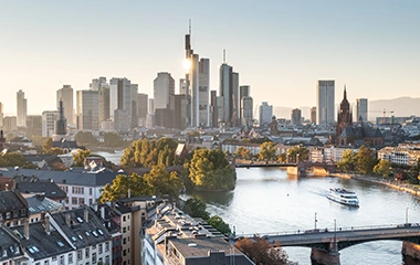 info-und-service-standorte-frankfurt Frankfurt: Luftaufnahme Frankfurts zeigt moderne Wolkenkratzer, Main mit Schiff und herbstliche Bäume in der City unter goldenem Sonnenuntergang.