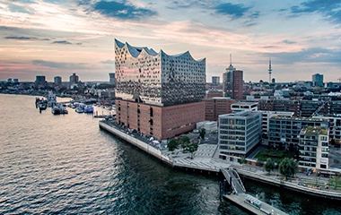 info-und-service-standorte-hamburg Frankfurt: Luftaufnahme Frankfurts zeigt moderne Wolkenkratzer, Main mit Schiff und herbstliche Bäume in der City unter goldenem Sonnenuntergang.