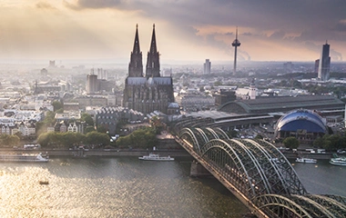 info-und-service-standorte-koeln Köln: Luftaufnahme Kölns mit Dom, Rhein und Hohenzollernbrücke bei warmer Abendsonne über der Altstadt.
