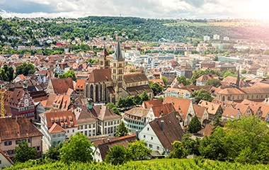 info-und-service-standorte-stuttgart Stuttgart: Luftaufnahme Stuttgarts mit historischer Altstadt, roten Ziegeldächern und grünen Hügeln bei warmem Sonnenlicht.