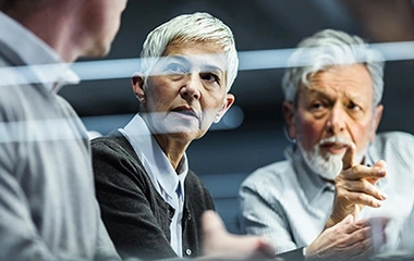 Gruppe im intensiven Austausch, Handgestik sichtbar, reflektierende Glasflächen betonen die sachliche Atmosphäre. Strategic Mind – Strategisch Denken